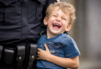 A preschool kid in the arms of a policeman laughs and laughs.